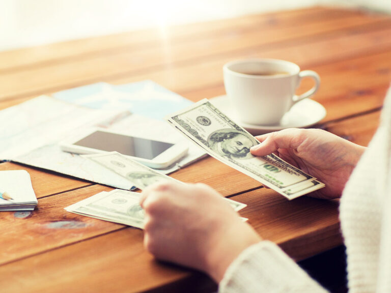 Hands counting money with business-related items on desk in background