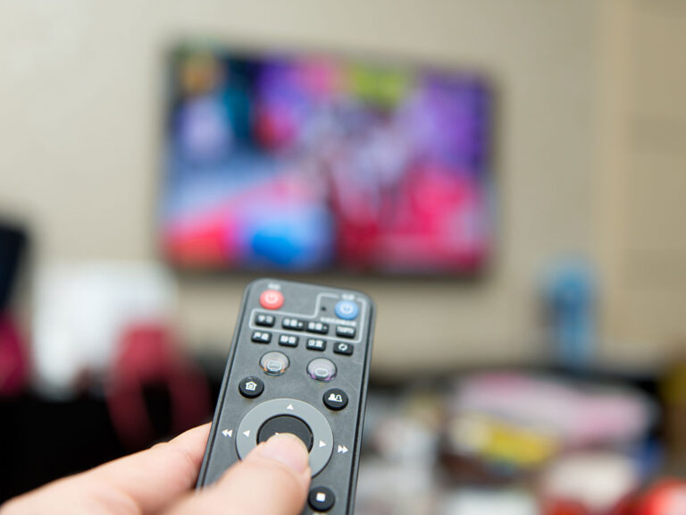 Hand holding remote control pointed at a TV on the wall